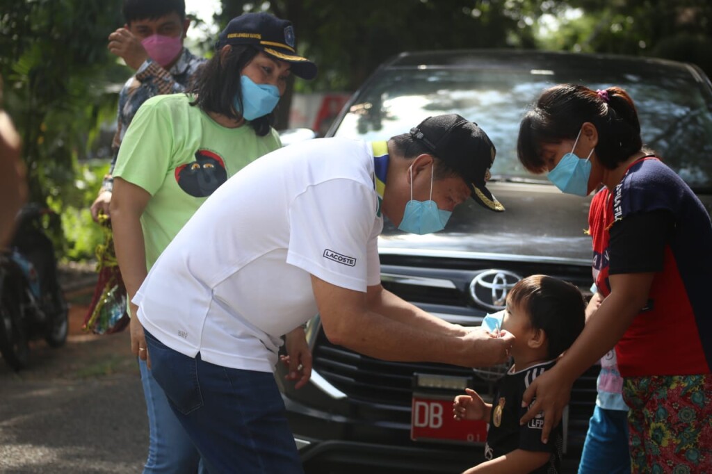 Walikota Max Lomban didampingi Ketua TP PKK Kota Bitung Khouni Lomban Rawung memakaikan masker pada seorang anak saat perjalanan ke tempat acara, Senin (10/08/2020)