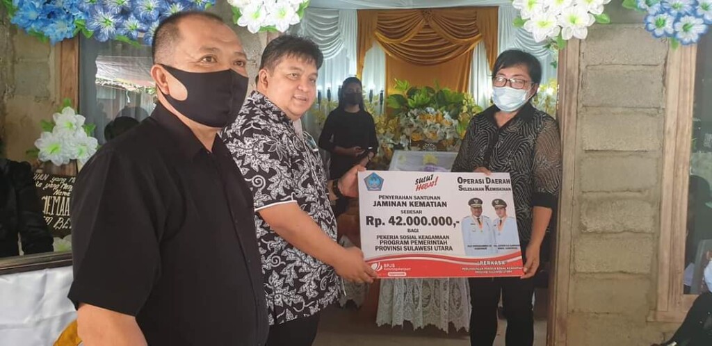 Gubernur Olly Dondokambey SE dan Wakil Gubernur Sulut Drs Steven OE Kandouw diwakili Kaban Kesbangpolda Sulut Evans Steven Liow S.Sos menyerahkan santuan jaminan kematian sebesar Rp42 juta kepada Titi Diamanti, istri sekaligus Ahli Waris Alm Jacob Diamanti, Minggu (30/08/2020)